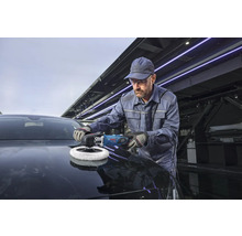 Ein Handwerker poliert die Motorhaube eines dunklen Autos mit einer professionellen Bosch Poliermaschine in einer Werkstatt.