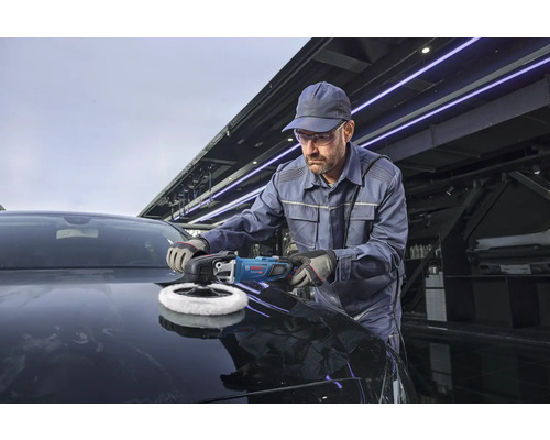 Ein Handwerker poliert die Motorhaube eines dunklen Autos mit einer professionellen Bosch Poliermaschine in einer Werkstatt.