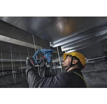 Handwerker befestigt mit einem Bosch Professional batteriebetriebenen Betonnagler Metallschienen an einer Betondecke auf einer Baustelle.