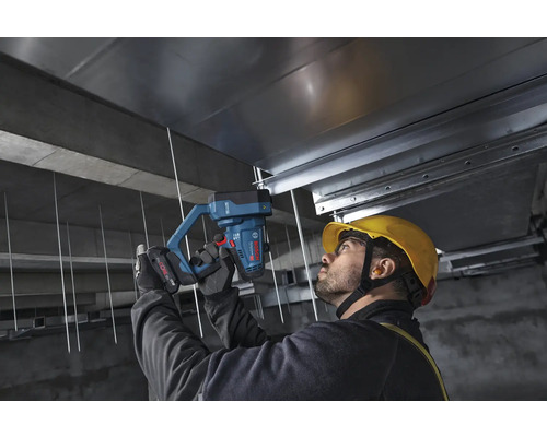 Handwerker befestigt mit einem Bosch Professional batteriebetriebenen Betonnagler Metallschienen an einer Betondecke auf einer Baustelle.