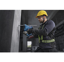 Bauarbeiter nutzt Bosch Akku-Bohrhammer mit Staubabsaugung an einer Betonwand, trägt Schutzausrüstung wie Helm und Brille.