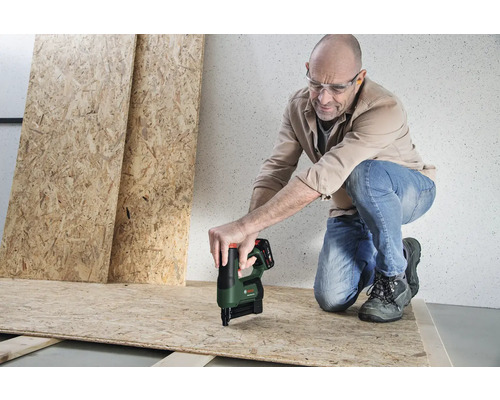 Ein Mann mit Schutzbrille befestigt eine OSB-Platte mit einem Akku-Tacker von Bosch auf einer Holzunterkonstruktion.