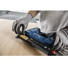 In einem hellen Arbeitsbereich lädt ein Handwerker in Handschuhen einen Nagelstreifen in einen Bosch Nagler mit Akkumulator auf Holz, Bosch Logo.