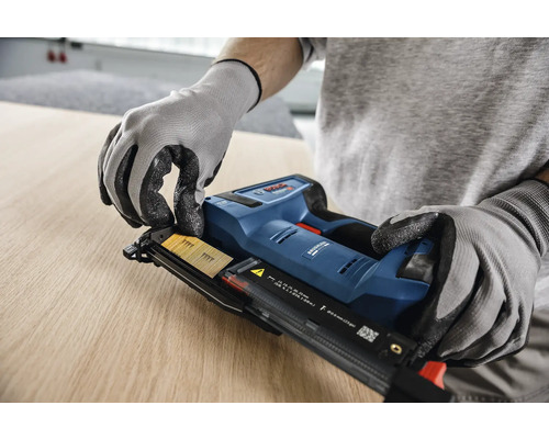 In einem hellen Arbeitsbereich lädt ein Handwerker in Handschuhen einen Nagelstreifen in einen Bosch Nagler mit Akkumulator auf Holz, Bosch Logo.