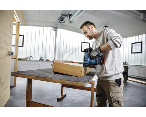 Handwerker montiert eine Holzschublade mit einem Akku-Tacker in einer hellen, organisierten Werkstatt.