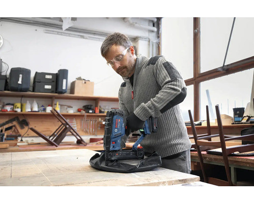 Handwerker nutzt Bosch Professional Akku-Tacker zur Polsterung eines Hockers in einer hellen Werkstatt.
