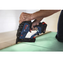 Eine Person verwendet einen Bosch Professional Akkumulator-Nagler zum Verlegen von Holzfußbodendielen auf einer Unterlage.