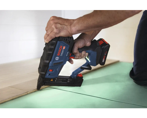 Eine Person verwendet einen Bosch Professional Akkumulator-Nagler zum Verlegen von Holzfußbodendielen auf einer Unterlage.