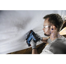 Handwerker befestigt Folie mit Bosch Akku-Tacker im Dachausbau, trägt Schutzbrille, Handschuhe und Gehörschutz.