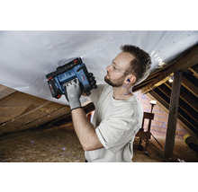 Mann befestigt mit einem Bosch Akkumulator-Tacker eine weiße Dampfbremsfolie an einer Holzkonstruktion im Dachgeschoss.