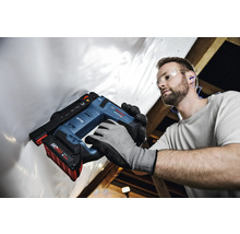 Handwerker mit Schutzausrüstung befestigt weiße Folie mit einem Bosch Professional Akku-Tacker an einer Dachkonstruktion aus Holz.
