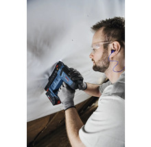 Handwerker verwendet einen Bosch Akku-Tacker mit Schutzbrille, Gehörschutz und Arbeitshandschuhen an einer weißen Folie.