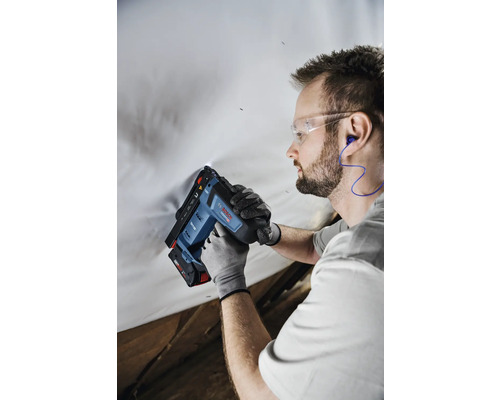 Handwerker verwendet einen Bosch Akku-Tacker mit Schutzbrille, Gehörschutz und Arbeitshandschuhen an einer weißen Folie.