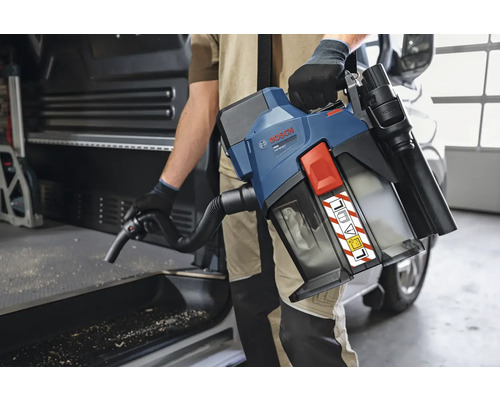 Eine Person verwendet einen Bosch Professional Akku-Staubsauger mit Schultergurt und Schlauch zur Reinigung von Sägespänen in einem Transporter.