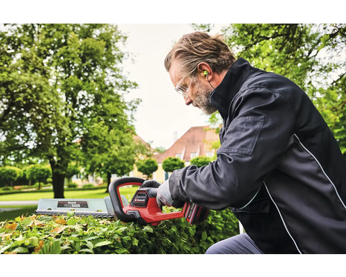 Mann schneidet Hecke mit einer elektrischen Heckenschere von Einhell im Garten.
