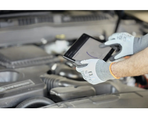Ein Mechaniker mit Schutzhandschuhen verwendet ein Tablet am Motor eines Autos.