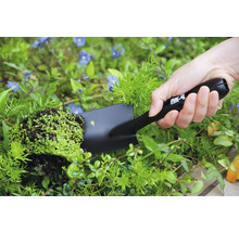 Person hält eine Handschaufel mit Pflanze im Garten.