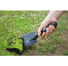Eine Person hält eine schwarze Gartenschaufel mit einem Stück Erde und Pflanzen in der Hand.