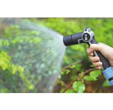 Eine Hand hält eine Gartenspritze, aus der Wasser auf Pflanzen gespritzt wird