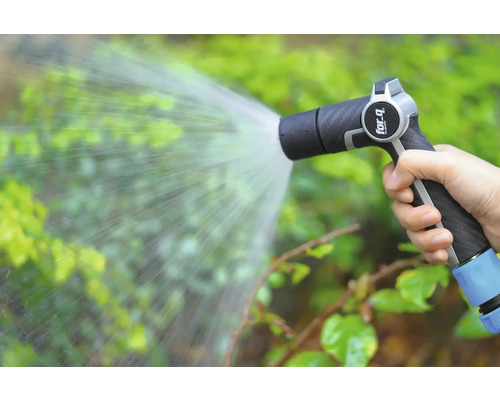 Eine Hand hält eine Gartenspritze, aus der Wasser auf Pflanzen gespritzt wird