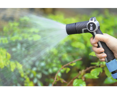 Eine Hand hält eine Gartenspritze und bewässert Pflanzen.