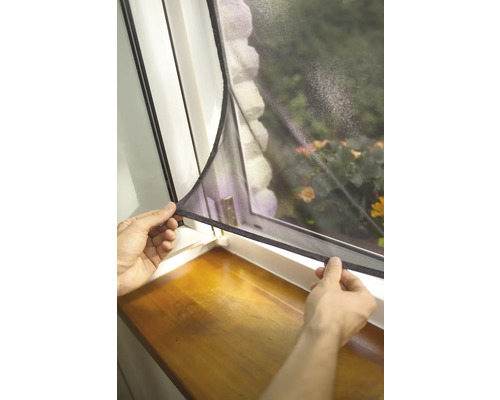 Person befestigt ein Insektenschutzgitter an einem Fenster.