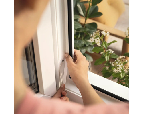Eine Person montiert eine Fensterdichtung an einem weißen Fensterrahmen.