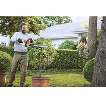 Mann schneidet Busch mit einer Heckenschere im Garten