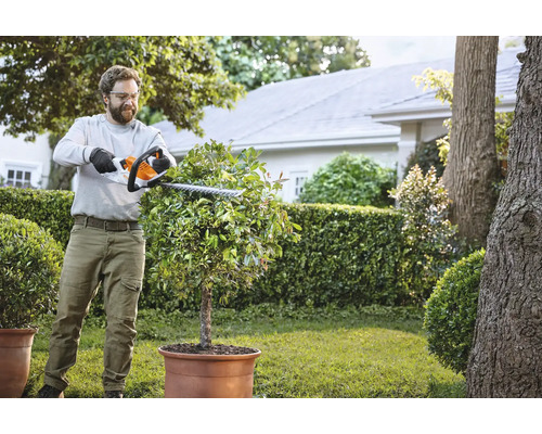 Mann schneidet Busch mit einer Heckenschere im Garten