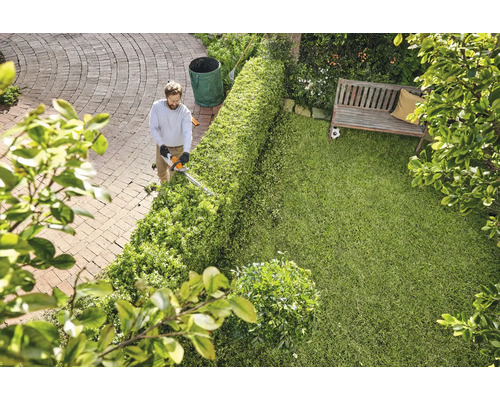 Mann schneidet Hecke mit Heckenschere in einem Garten.
