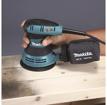 Makita Exzenterschleifer beim Schleifen eines Holzbretts mit Staubfangsack.
