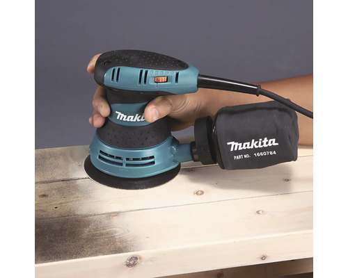 Makita Exzenterschleifer beim Schleifen eines Holzbretts mit Staubfangsack.