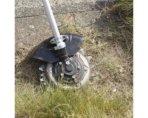 Rotations-Unkrautbürste mit Metallklingen im Einsatz auf einer Rasenfläche mit trockenem Gras.
