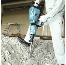 Makita Abbruchhammer wird von einer Person in Arbeitskleidung auf einem Haufen aus Betonschutt verwendet.