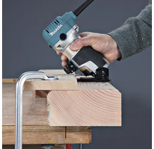 Eine Person bearbeitet die Kante eines auf einer Werkbank fixierten Holzbretts mit einer Makita Einhandfräse.