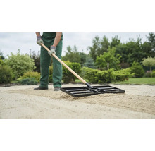 Eine Person ebnet Sand mit einer Einebnungsharke im Garten.