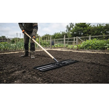 Eine Person ebnet den Gartenboden mit einem Planierschild vor dem Bepflanzen.