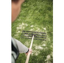 Eine Person verteilt Rasendünger mit einem Rasenstreuer auf einer Rasenfläche.