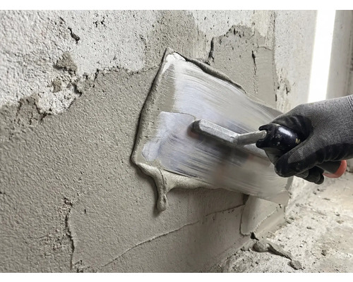 Eine Person glättet Putz mit einer Glättkelle an einer Wand.