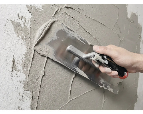 Maurer verputzt Wand mit Glättekelle