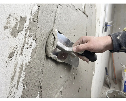 Handwerker trägt Putz mit einer Glättkelle auf eine Wand auf.