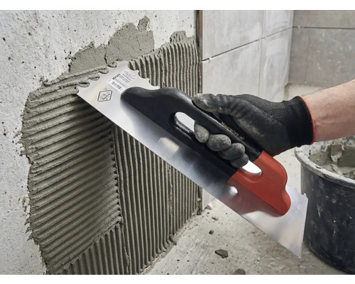 Aufbringen von Fliesenkleber mit einer rostfreien Stahltraufel auf eine Wand