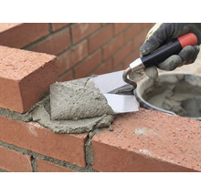 Maurer verarbeitet Ziegel mit einer Kelle und Mörtel.