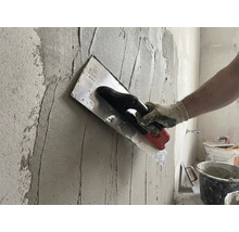 Handwerker trägt Putz mit einer Glättkelle auf eine Wand auf.