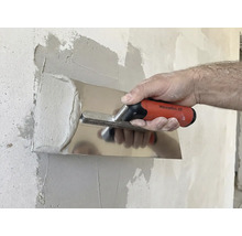 Eine Person glättet Putz mit einer Glättkelle an einer Wand.