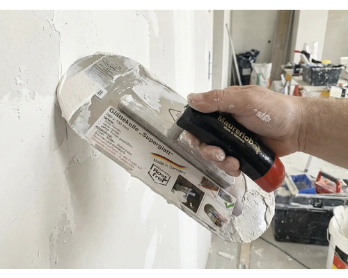 Glättkelle Superglatt mit Griff in der Hand beim Verputzen einer Wand