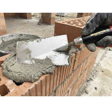 Maurer mit Kelle beim Auftragen von Mörtel auf Ziegelsteine für Mauerbau