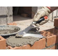 Maurerhand mit Kelle beim Auftragen von Mörtel auf Ziegelsteine