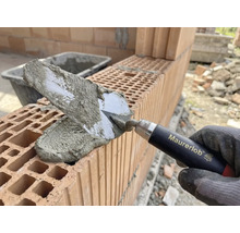 Maurerhand mit Maurerkelle beim Auftragen von Mörtel auf Ziegelsteine