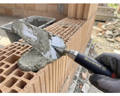 Maurerhand mit Maurerkelle beim Auftragen von Mörtel auf Ziegelsteine